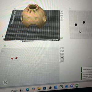 Könnte beinhalten: Ein digitales 3D-Modell eines abgerundeten, knödelartigen Objekts mit texturierter Oberfläche, das eine kleine kreisförmige Öffnung an der Oberseite, zwei seitliche Aussparungen und ein lächelndes Gesicht auf einer Softwareoberfläche zeigt.