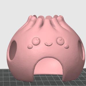 May include: A light pink, rounded, hollow ceramic-style object with a pleated top, featuring a smiling face with two large circular eyes and a small curved mouth, and three arched openings at the base and sides for ventilation or access.
