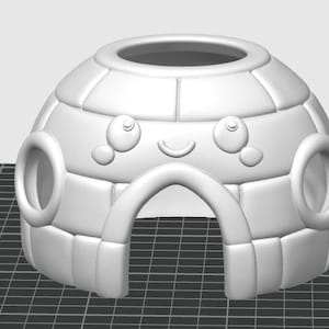 May include: A white igloo-shaped structure featuring a dome design with block-like segments. The front displays a carved face with two circular eyes, two small circular cheeks, and a curved mouth above a central arched doorway opening.