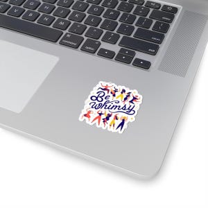 May include: A sticker with the words "Be Whimsy" in dark blue script, surrounded by dancing figures in various colors. The sticker is on a laptop.