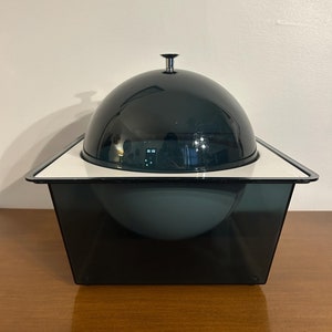 May include: A black and white ice bucket with a dome lid. The lid has a small knob on top. The ice bucket is made of plastic and has a square base.