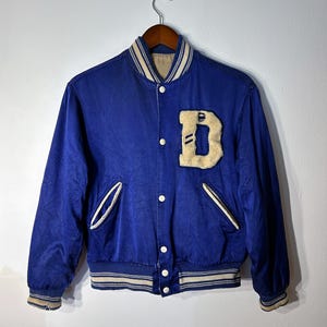 May include: A blue satin varsity jacket with a white and blue striped collar and cuffs. The jacket has a large felt letter 'D' on the left chest.