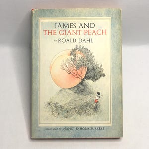 May include: A vintage hardcover book titled "JAMES AND THE GIANT PEACH" by Roald Dahl. The cover features an illustration of a large peach, a tree, and a small figure. The book is illustrated by Nancy Ekholm Burkert.