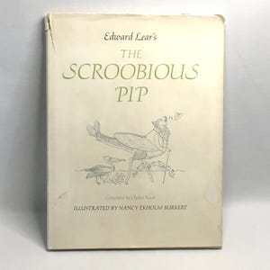 May include: A hardcover book titled Edward Lear's The Scroobious Pip, completed by Ogden Nash and illustrated by Nancy Ekholm Burkert. The off-white cover features a central line drawing of a fantastical creature with wings and a fish tail.