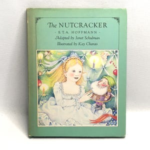 May include: A hardcover book titled The Nutcracker by E.T.A. Hoffmann, adapted by Janet Schulman and illustrated by Kay Chorao. The light green cover features a central illustration of a young person with blonde hair holding a small nutcracker doll.