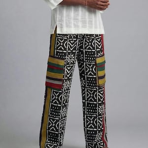 May include: Patterned trousers in black and white with geometric patterns and colourful accents. The trousers have cargo pockets with red, green, and yellow stripes. They are worn with a white, long-sleeved shirt.