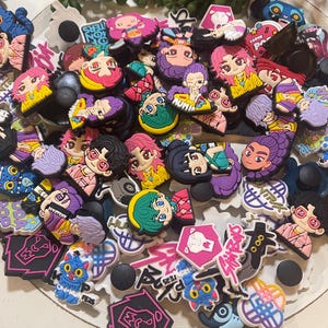 Pu&ograve; includere: Una collezione di ciondoli colorati per scarpe con personaggi in stile anime con vari acconciature e abiti. Alcuni ciondoli hanno testo, tra cui "ION HUNTERS" e "I LOVE POP". I ciondoli sono in tonalit&agrave; di rosa, viola, giallo e blu.