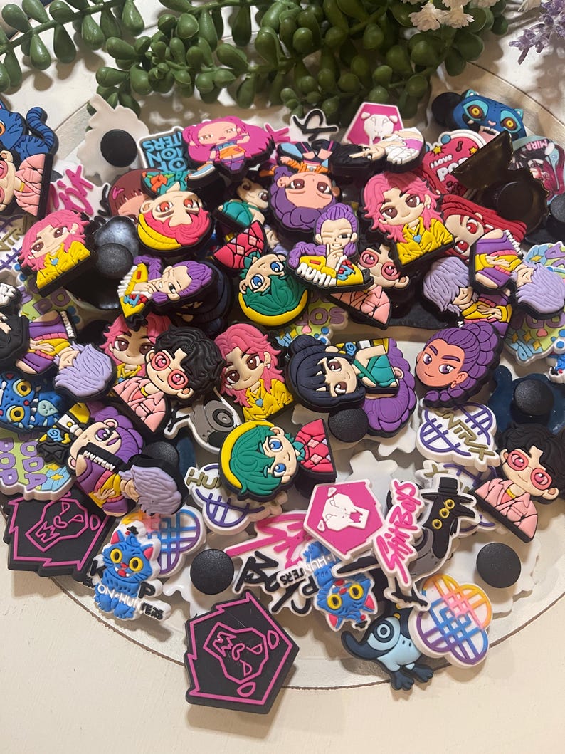 Pu&ograve; includere: Una collezione di ciondoli colorati per scarpe con personaggi in stile anime con vari acconciature e abiti. Alcuni ciondoli hanno testo, tra cui "ION HUNTERS" e "I LOVE POP". I ciondoli sono in tonalit&agrave; di rosa, viola, giallo e blu.