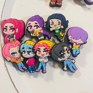 Pu&ograve; includere: Una collezione di ciondoli di personaggi dei cartoni animati colorati. I ciondoli presentano vari personaggi con diversi colori di capelli, abiti ed espressioni. I ciondoli sono realizzati in un materiale gommoso e sono probabilmente per scarpe o accessori.