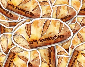 May include: A collection of stickers featuring a watercolor illustration of a loaf of sourdough bread. The bread is golden brown with a textured crust and the text "In My Sourdough Era" in a dark brown font.