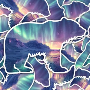 May include: A white-outlined bear sticker with a landscape of mountains, water, and an aurora borealis sky in shades of purple, blue, green, and orange. The sticker has a white border and a repeating pattern.