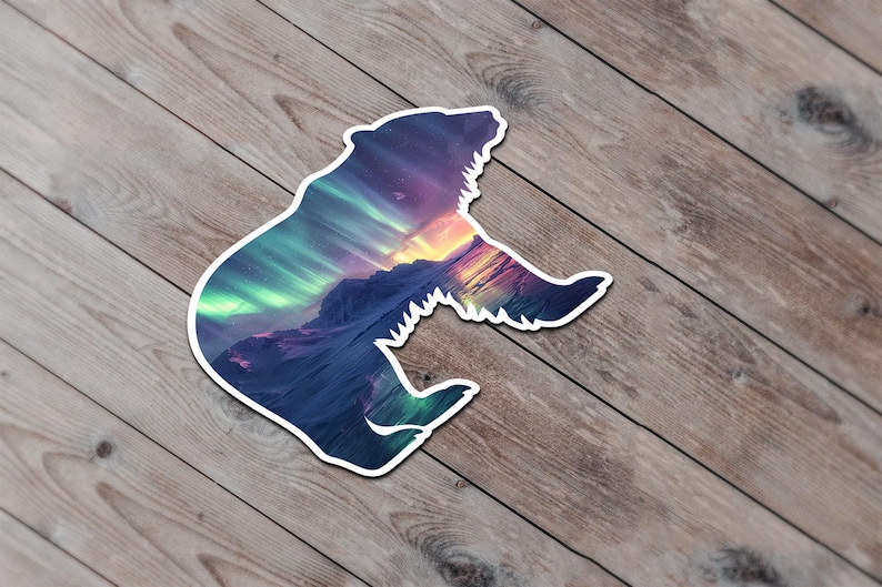 May include: A bear-shaped sticker with a white border, depicting a vibrant mountain landscape and aurora borealis. The sticker is set against a wooden background.