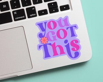 May include: A sticker with the phrase "You Got This" in purple, pink, and white lettering, with a small flower graphic. The sticker is on a laptop, with a light blue background.