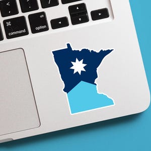 May include: A sticker in the shape of the state of Minnesota, with a dark blue upper portion and a light blue lower portion. A white star is in the center of the dark blue area. The sticker is on a laptop.