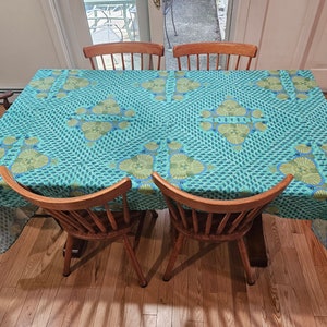 May include: A blue and green patterned tablecloth with a geometric design covers a wooden table with four wooden chairs.