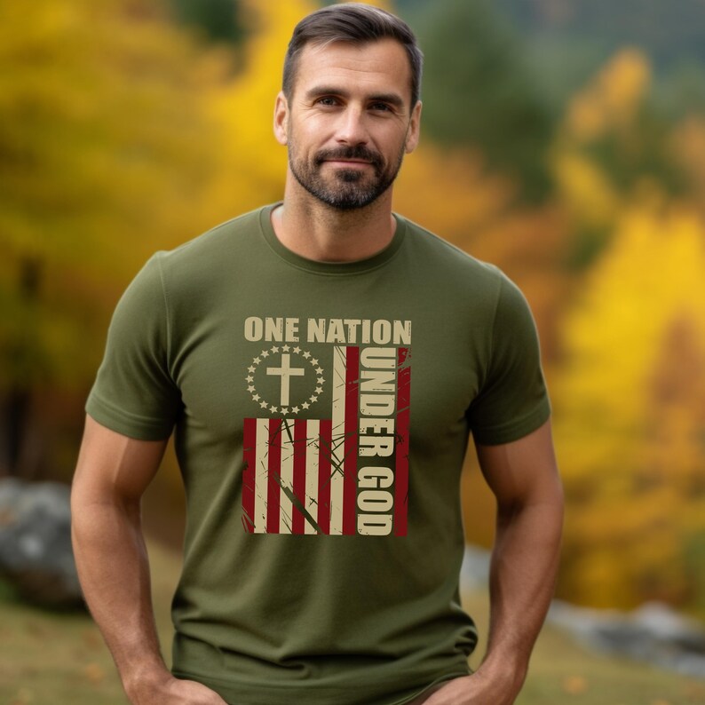 May include: Olive green t-shirt with the text "ONE NATION UNDER GOD" and a distressed American flag design. The flag features a cross, stars, and red and white stripes. The shirt is short-sleeved.