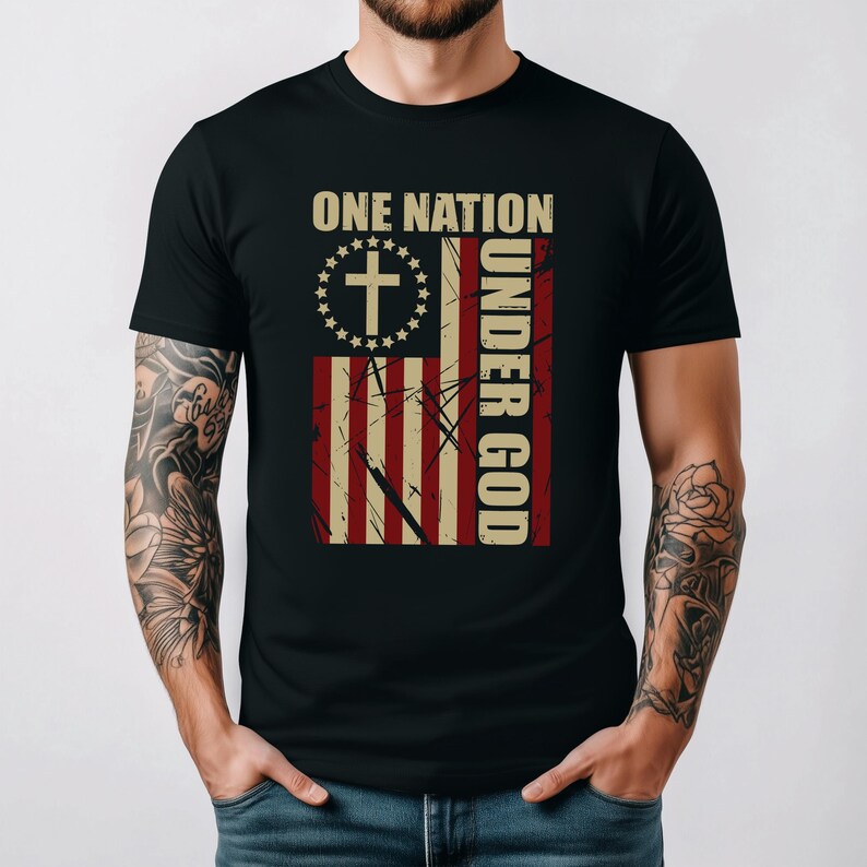 May include: Black t-shirt with a distressed American flag design and the text "ONE NATION UNDER GOD." The flag includes a cross and stars, with vertical text on the right. The shirt has a classic crew neck.