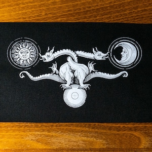 May include: A black patch with a white design of a three-headed dragon holding a sun, moon, and a circle in its claws.