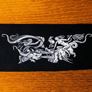 May include: Black fabric patch with a white design of two figures riding mythical creatures. One figure is riding a winged creature with a long tail, while the other figure is riding a creature with a long, flowing mane.