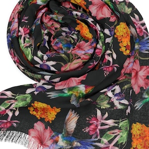 May include: A black scarf with a vibrant floral pattern featuring pink, orange, and purple flowers, and green hummingbirds. The scarf has a fringed edge. The scarf is rolled up, displaying the intricate design.