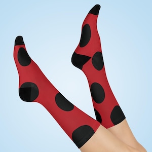 May include: Red socks with large black polka dots, resembling a ladybug pattern. The socks have black heels and toes. The socks are shown on a light blue background.