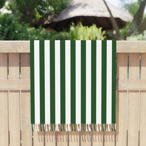 May include: A rectangular towel featuring a repeating vertical striped pattern in dark forest green and crisp white. The bottom edge of the towel is finished with a row of short, knotted fringe tassels in matching green and white colors.