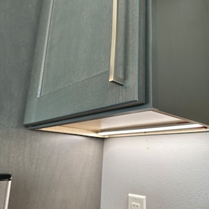 May include: A gray cabinet with a silver handle and a white light strip underneath. The light strip is mounted on a white wall.