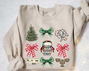 May include: A beige sweatshirt with a Christmas theme featuring a Christmas tree, bows, lights, a camper, a moose, and the text "You Serious Clark?"