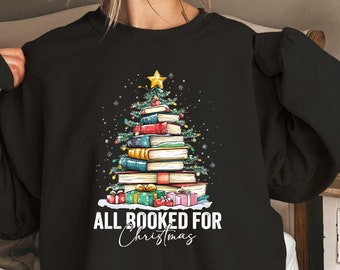 May include: Black sweatshirt with a Christmas tree made of stacked books. The tree is decorated with ornaments and a star on top. The text "All Booked for Christmas" is printed below the tree.