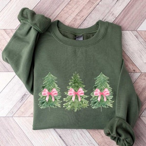May include: A green sweatshirt with a Christmas tree design. The trees are decorated with pink bows.