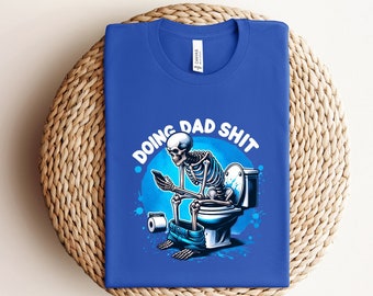 May include: A blue t-shirt with a skeleton sitting on a toilet and holding a phone. The text "Doing Dad Shit" is printed on the shirt.