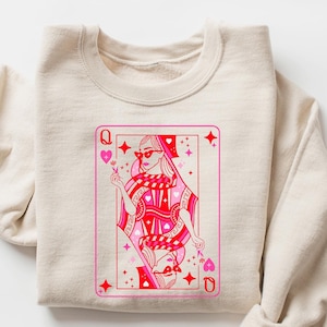 May include: A sand-colored sweatshirt with a pink and red Queen of Hearts playing card graphic. The graphic features a woman wearing sunglasses and a crown.
