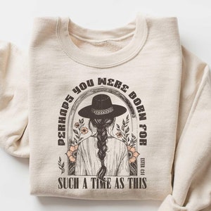 May include: A beige sweatshirt with a graphic print of a woman wearing a cowboy hat and the text "Perhaps you were born for such a time as this".