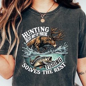 May include: A dark gray t-shirt with a distressed look featuring a graphic of a deer jumping out of the water with a fish. The text on the shirt reads "Hunting solves most my problems Fishing solves the rest".