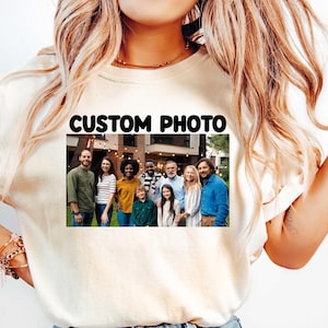 May include: A cream-colored t-shirt featuring a rectangular graphic print on the chest. The print displays the text CUSTOM PHOTO above a color photograph of a diverse group of nine people standing together outdoors in front of a building.
