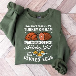 May include: Green sweatshirt with the text "I wouldn't do much for turkey or ham but I would do some sketchy shit for deviled eggs." The graphic includes illustrations of a turkey, ham, and deviled eggs.