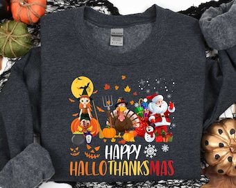 May include: A dark gray sweatshirt with a festive design featuring a witch, a turkey, Santa Claus, and pumpkins. The text "Happy HalloThanksmas" is printed in red, orange, and yellow on the front of the sweatshirt.