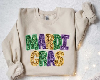 May include: A beige sweatshirt with the words "Mardi Gras" in green, purple, and gold glitter letters.