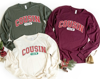 Puede incluir: Tres camisas de manga larga con el texto "COUSIN CREW" en rojo y verde sobre un fondo blanco, verde y burdeos.