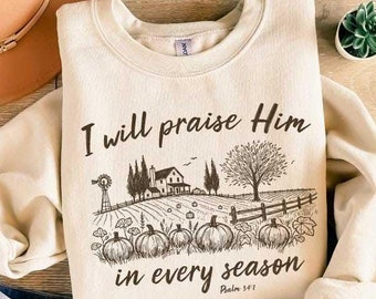 May include: A cream-colored sweatshirt with a brown graphic of a farmhouse and pumpkins. The text "I will praise Him in every season Psalm 33:1" is printed on the sweatshirt.