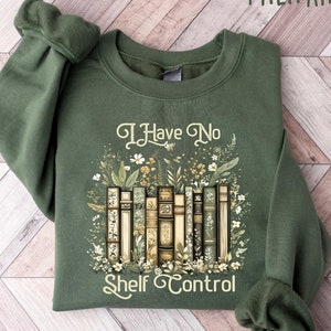 May include: Military green sweatshirt with the text "I Have No Shelf Control" and a graphic of vintage books surrounded by floral elements. The long-sleeved crew neck top is made of a soft material.