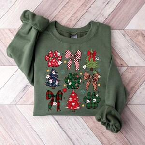 May include: Green sweatshirt with a Christmas-themed design featuring paw prints, bows, and Christmas trees. The design is in red, green, and white.