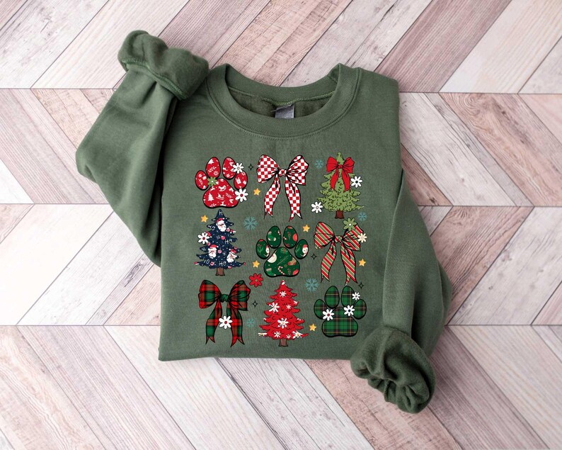 May include: Green sweatshirt with a Christmas-themed design featuring paw prints, bows, and Christmas trees. The design is in red, green, and white.
