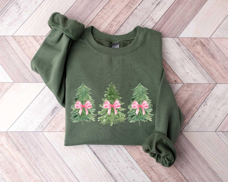 May include: A green sweatshirt with a Christmas tree design. The trees are decorated with pink bows.