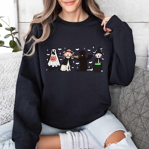 May include: A navy blue sweatshirt featuring a Halloween-themed graphic. The graphic depicts four dogs dressed in costumes: a ghost, a witch, a vampire, and a witch with a cauldron. The design includes bats and stars.