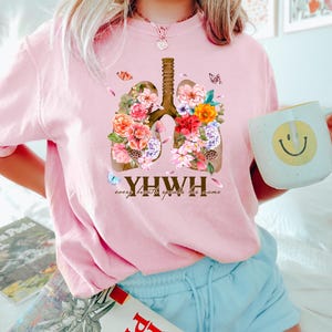 May include: Pink t-shirt with a floral design of lungs and the text "YHWY every breath speaks his name".