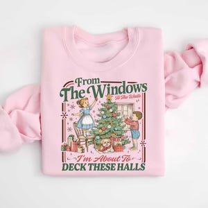 May include: Pink sweatshirt with a vintage Christmas graphic. The design features a Christmas tree, children decorating, and the text "From The Windows To The Walls, I'm About To Deck These Halls."