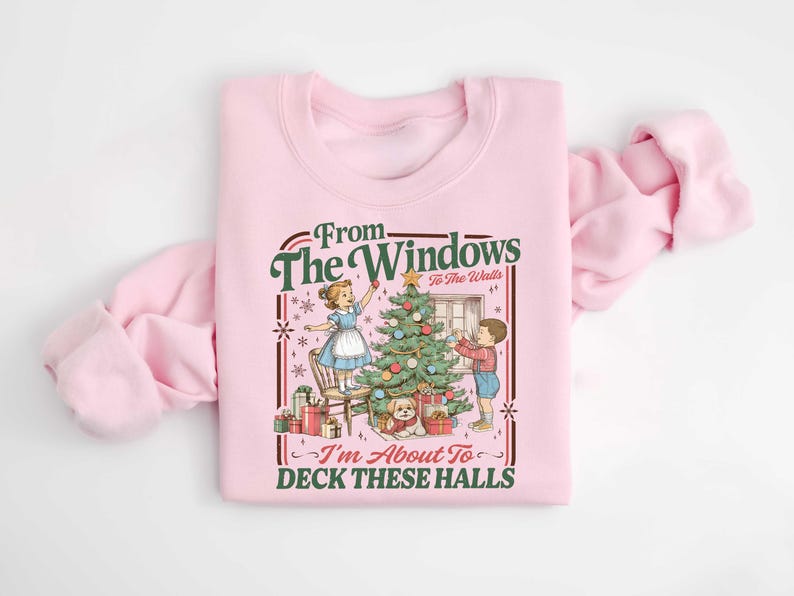 May include: Pink sweatshirt with a vintage Christmas graphic. The design features a Christmas tree, children decorating, and the text "From The Windows To The Walls, I'm About To Deck These Halls."