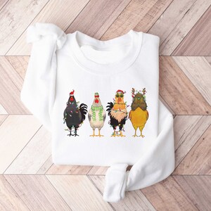 May include: White sweatshirt with a graphic of four roosters wearing Christmas lights and hats. The roosters are in a line, facing forward.