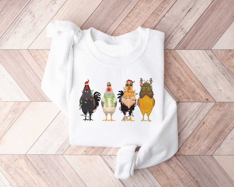 May include: White sweatshirt with a graphic of four roosters wearing Christmas lights and hats. The roosters are in a line, facing forward.